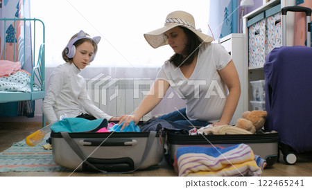 In a cozy room, a mother and daughter pack a suitcase for their summer vacation, folding clothes and organizing outfits together In a cozy room, a mother and daughter pack a suitcase for their summer vacation, folding clothes and organizing outfits together 122465241