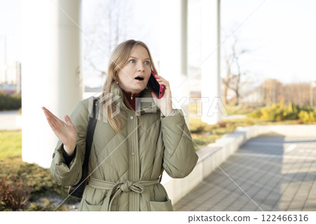 Portrait of beautiful shocked young woman talking on the mobile as she getting terrible news on the city street Portrait of beautiful shocked young woman talking on the mobile as she getting terrible news on the city street 122466316
