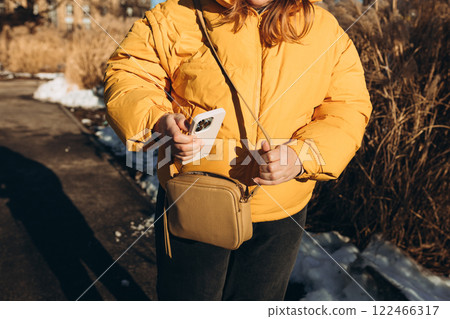 Closeup of woman's hands taking out smartphone from purse outdoors. Young stylish woman taking cellphone out of handbag. Crop anonymous female putting modern cellphone into fashionable handbag 122466317