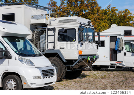 Big off-road expedition truck parked many white modern campervan recreational motor home vehicles in row camper park site Magdeburg city. Motorhome campground station travel destination. RV lifestyle 122466334