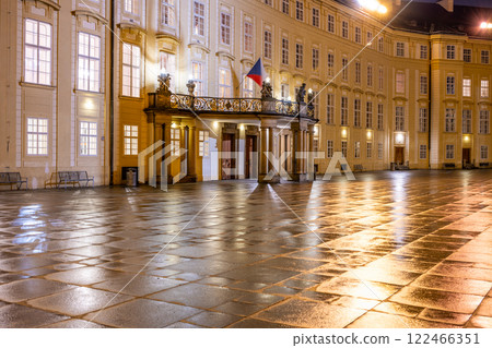 The impressive entrance door to Prague Castle glows under evening lights, with a beautiful balcony adorned by the Czech flag and a reflective courtyard after rain. The impressive entrance door to Prague Castle glows under evening lights, with a beautiful balcony adorned by the Czech flag and a reflective courtyard after rain. 122466351