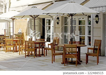 Wooden cafe tables and chairs with parasols line the courtyard, which is designed mainly in white. 122466515
