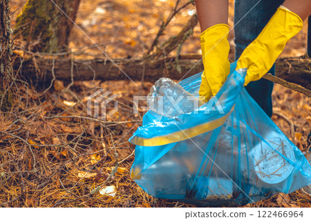 A woman fights to save the forest from garbage. A woman with a garbage bag in her hands collects plastic waste in the forest. Ecology, saving nature from plastic waste. A woman fights to save the forest from garbage. A woman with a garbage bag in her hands collects plastic waste in the forest. Ecology, saving nature from plastic waste. 122466964