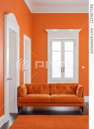 A living room sofa is positioned against an orange wall, with a white classic door in background A living room sofa is positioned against an orange wall, with a white classic door in background 122467348