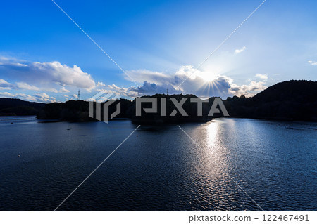 Evening scenery at Nara Nunome Dam as the cold weather returns. From sunset to the end of the sunset, the sun shines and a path of light forms on the lake surface. Evening scenery at Nara Nunome Dam as the cold weather returns. From sunset to the end of the sunset, the sun shines and a path of light forms on the lake surface. 122467491