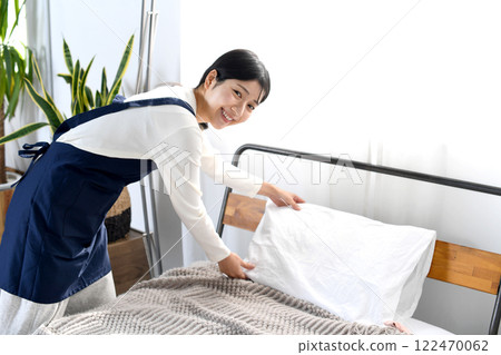 一個穿著圍裙的女人正在整理床鋪 122470062