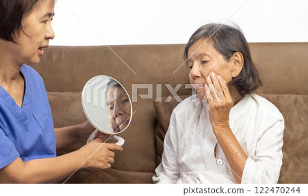 Elderly woman applying face powder with care giver in nursing home. Elderly woman applying face powder with care giver in nursing home. 122470244