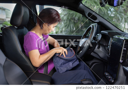 Senior asian woman sitting on drivers seat and look for a key inside handbag. 122470251