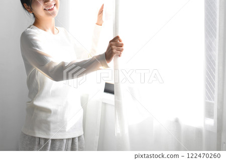 Asian woman opening the curtains and basking in the sunlight 122470260