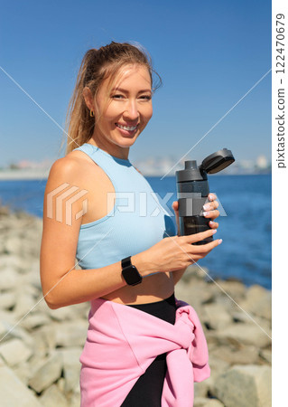 Smiling young blonde woman jogger runner drink water from bottle at river embankment closeup 122470679