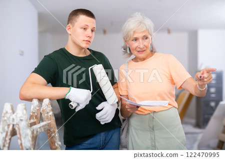 Mature woman shows a fifteen-year-old worker, a house repair plan on paper 122470995