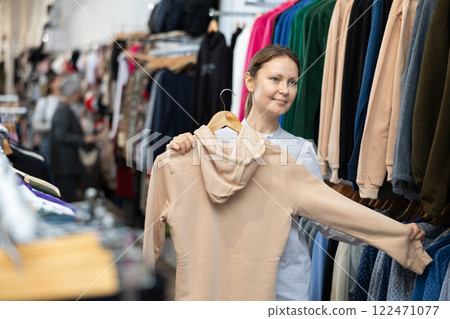 Woman shopping in clothing store with coats and cardigans 122471077