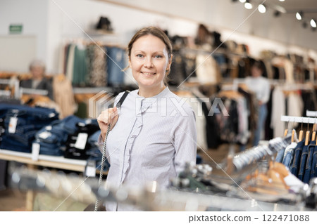 Middle-aged woman watching excitedly large stock of clothes in clothing store Middle-aged woman watching excitedly large stock of clothes in clothing store 122471088