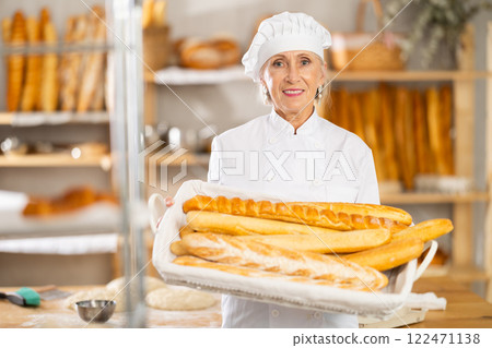 Senior female baker worker shows baguette 122471138