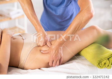 Image showcases close-up of mature female masseur hands skillfully working on things hip of woman 122471142