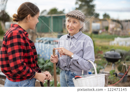Female farmers friendly talking outside next to wooden fence on background with farm Female farmers friendly talking outside next to wooden fence on background with farm 122471145
