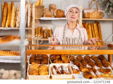 Selling fresh croissants in bakery - smiling female baker places hot croissants on display Selling fresh croissants in bakery - smiling female baker places hot croissants on display 122471146