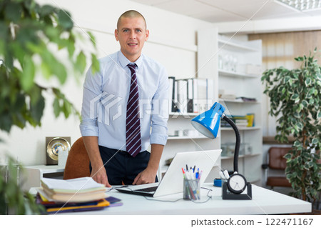 Office worker standing in workplace and looking in camera Office worker standing in workplace and looking in camera 122471167