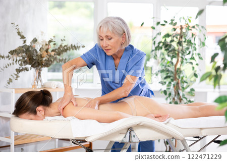 Elderly woman doing back massage to young woman 122471229