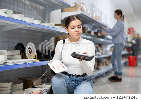 Young woman in supermarket is choosing square plates 122471243