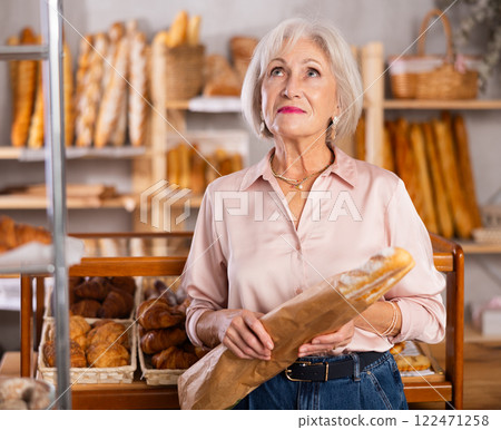 Elderly woman holds baguette wrapped in paper bag in bakery store 122471258