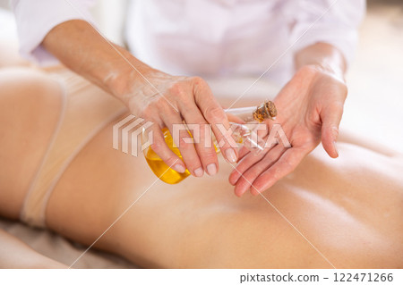 Elderly female masseur hands pours massage oil into palm of hand to soften clients skin. Close up 122471266