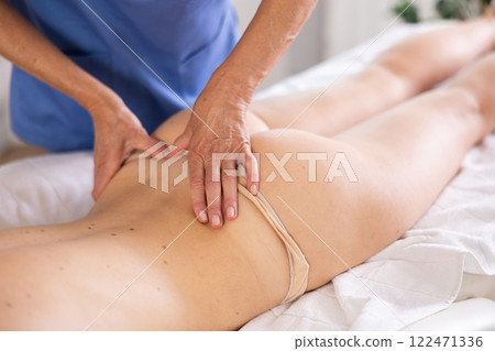 Masseuse doing back massage to young woman Masseuse doing back massage to young woman 122471336