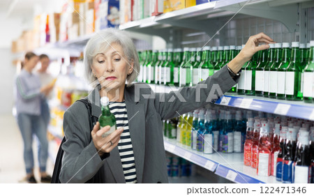 Elderly woman examining labels on bottles of soju in Asian store 122471346
