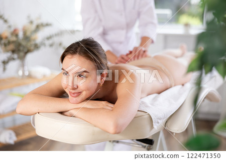 Vague mature woman actively rubs buttocks of young woman during general massage procedure. 122471350