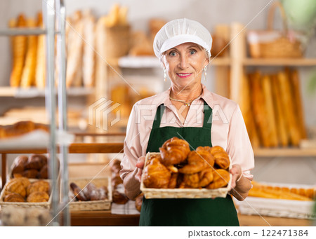 senior bakery worker sells croissants and shows off a variety of crescent-shaped buns. 122471384
