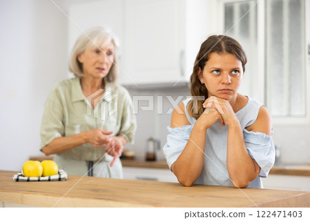 Senior woman scolding her adult daughter cooking breakfast in modern kitchen Senior woman scolding her adult daughter cooking breakfast in modern kitchen 122471403