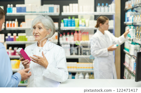 Senior woman apothecary hold package with cream and talks with man client about nuances of care 122471417