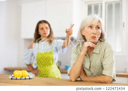 Offended senior woman at kitchen and listening daughter swearing. Offended senior woman at kitchen and listening daughter swearing. 122471434