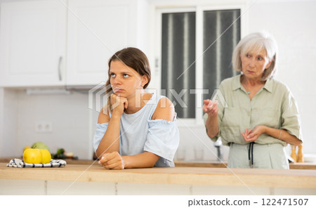 Senior woman scolding her adult daughter cooking breakfast in modern kitchen 122471507