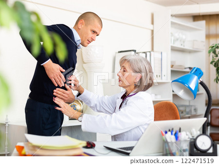 Senior female doctor palpating abdomen of male patient 122471519
