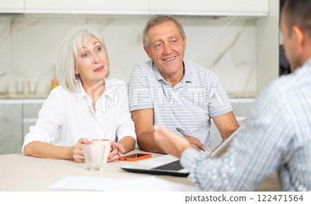 Salesman seller shows on laptop details of purchase to elderly couple. 122471564