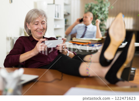 Carefree aged businesswoman playing online game on smartphone during business hours 122471623