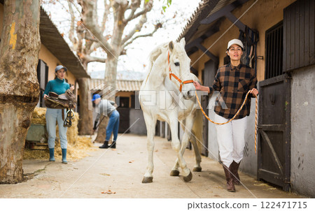 Women ranchers preparing white horse for ride Women ranchers preparing white horse for ride 122471715
