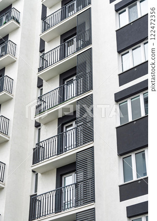 Close-up of a modern apartment building facade with black railings, white and grey tones, showcasing urban housing architecture design 122472356