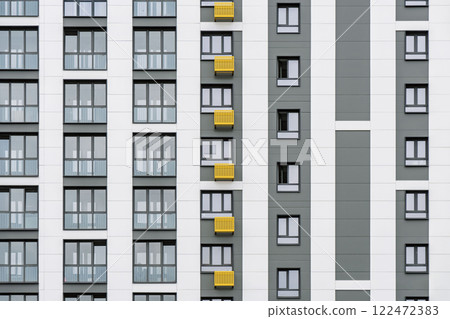 Contemporary building facade with yellow and grey accents, minimalist design, windows, and balconies, against a cloudy sky, front close view Contemporary building facade with yellow and grey accents, minimalist design, windows, and balconies, against a cloudy sky, front close view 122472383