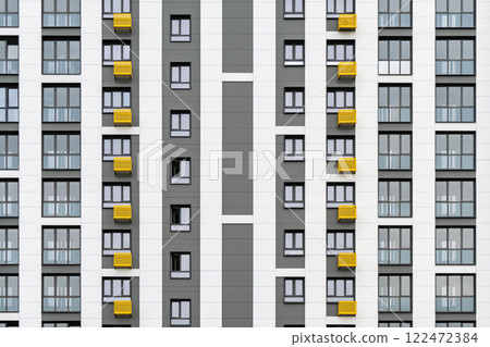 Contemporary building facade with yellow and grey accents, minimalist design, windows, and balconies, against a cloudy sky, front close view 122472384
