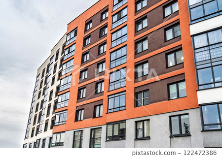 Modern apartment building facade, featuring beige, orange, and brown tones, with dark-framed windows, low angle view. Urban housing concept 122472386