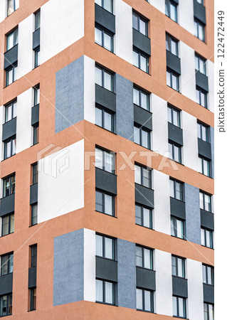 Modern apartment building facade, featuring orange, white and grey tones, with dark-framed windows with colorful accents. Urban housing concept 122472449