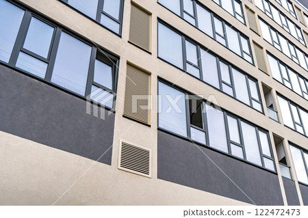 Modern building facade with large dark-framed windows and ventilation panels, showcasing clean architectural lines. Urban architecture concept Modern building facade with large dark-framed windows and ventilation panels, showcasing clean architectural lines. Urban architecture concept 122472473
