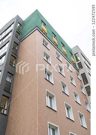 Contemporary building with brick facade, green rooftop, yellow accents, against bright sky. Urban architecture concept low angle view Contemporary building with brick facade, green rooftop, yellow accents, against bright sky. Urban architecture concept low angle view 122472595