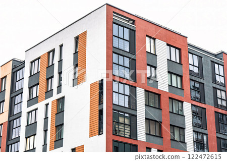 Modern apartment building facade, featuring white, orange, and red tones, with dark-framed windows, low angle view. Urban housing concept 122472615