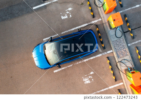 Blue electric car receives electricity at parking lot with charging station stands upper view. Modern eco-friendly auto reveals benefit of low cost fuel 122473243
