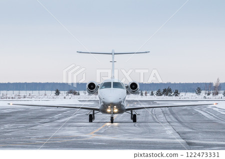 Front view of the modern white private jet taxiing on airport taxiway in winter 122473331
