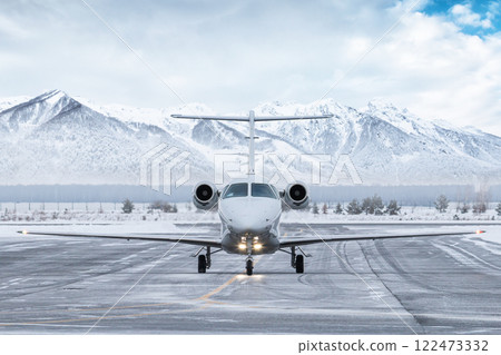 Front view of the white business jet taxiing on airport taxiway in winter on the background of high scenic snow capped mountains 122473332