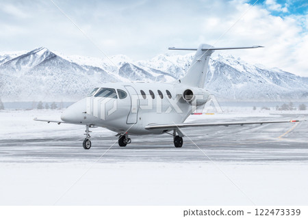 White private jet taxiing on airport taxiway in winter on the background of high picturesque snow capped mountains White private jet taxiing on airport taxiway in winter on the background of high picturesque snow capped mountains 122473339